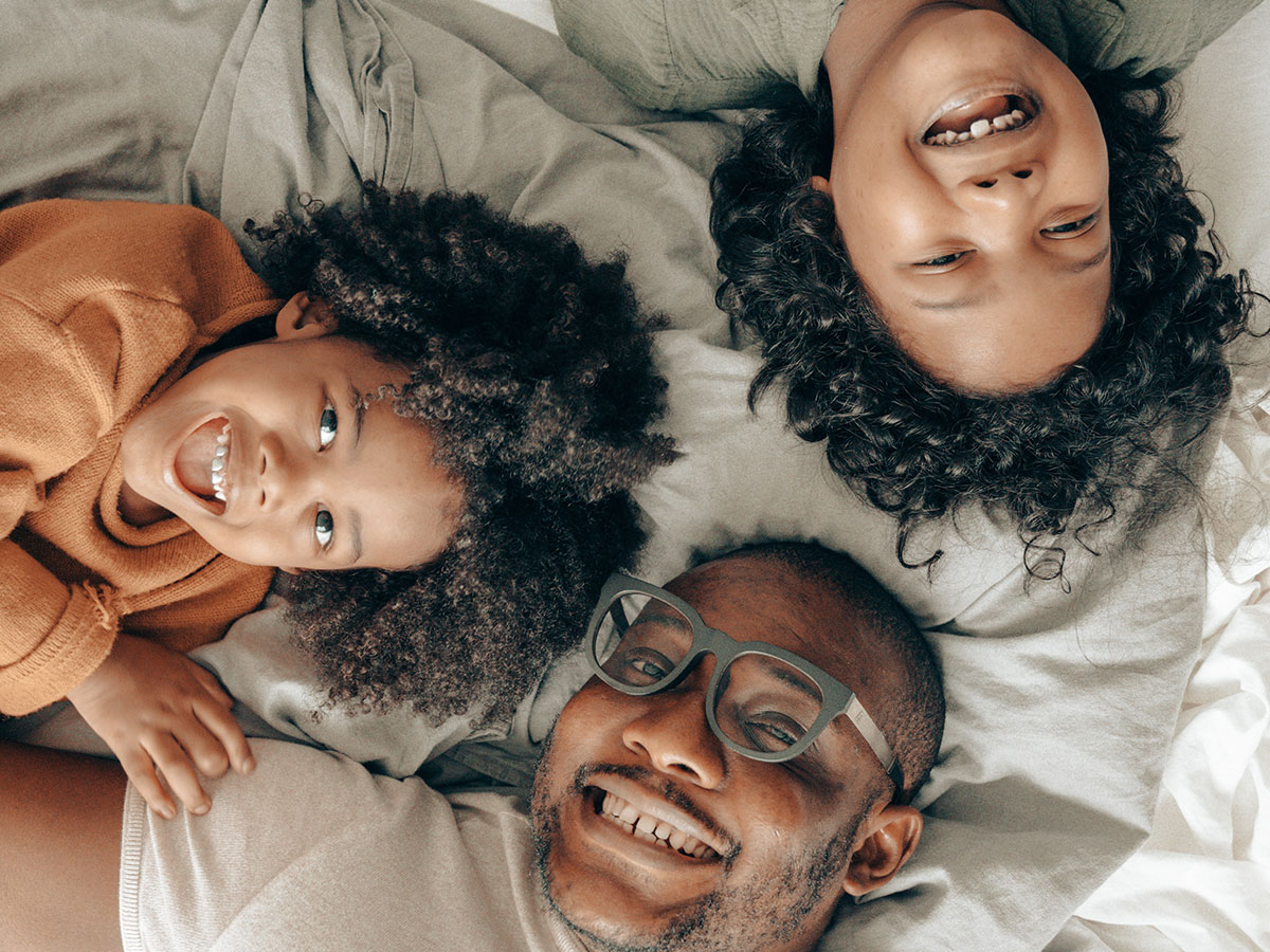 Black family laughing and smiling while lying on bed.