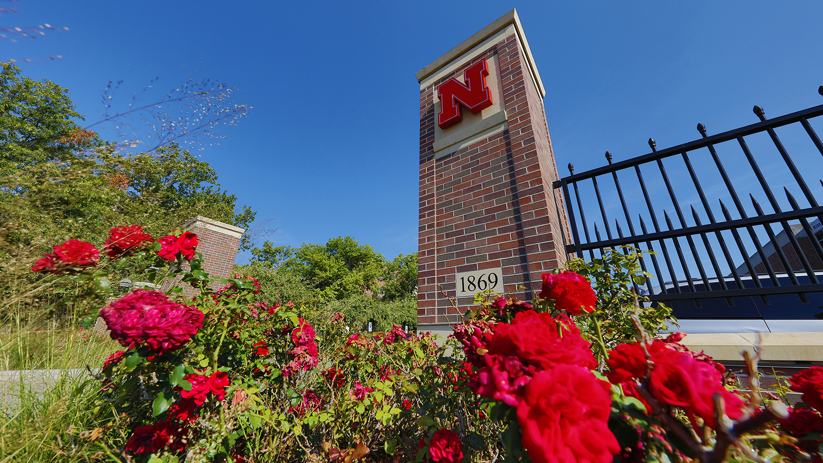 East Campus gateway with Nebraska N on pilar and red flowers in foreground