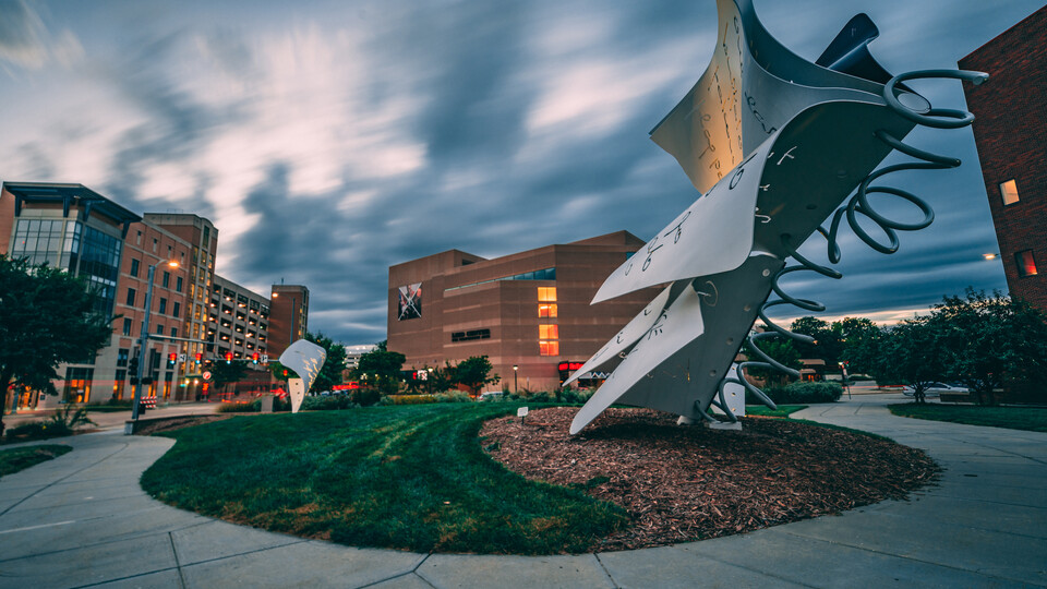 Image captured at dusk of greenspace, silver architectural sculptures and the Lied Center in downtown Lincoln. 