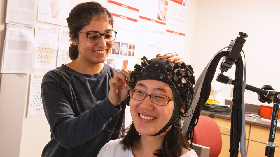 From left, student worker Randa Ismail adjusts a functional near-infrared spectroscopy cap on Grace Oh.