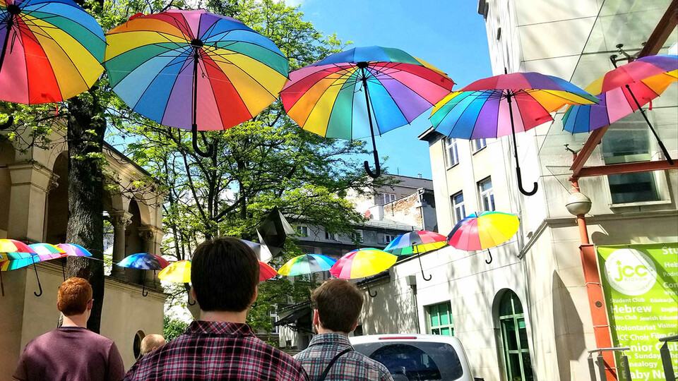 Colorful umbrellas hang over an ally in Krakow, Poland as students walk through on a sunny day during a study abroad trip in 2019.