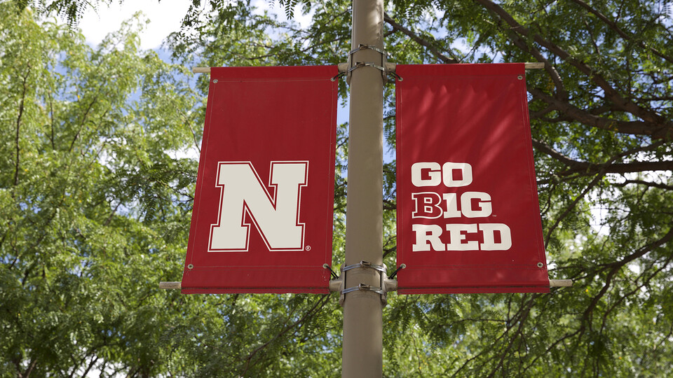 Two red ribbon banners hanging outdoors near green, leafy trees. One has an N on it and the other says Go Big Red. 