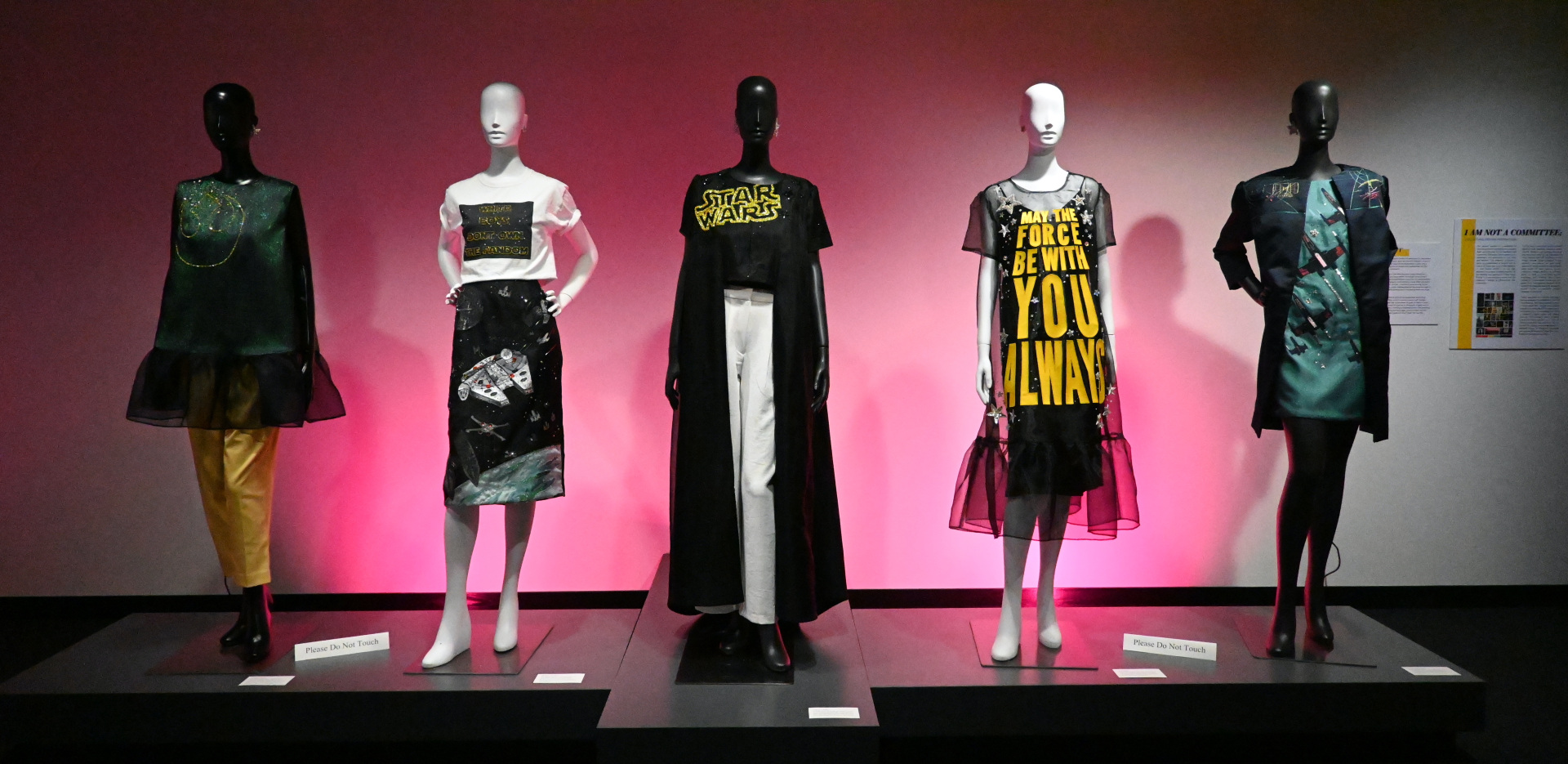 Five mannequin's on display dressed in garments from "A Woman's Place is in the Resistance." The display is backlit in a pink shade. 