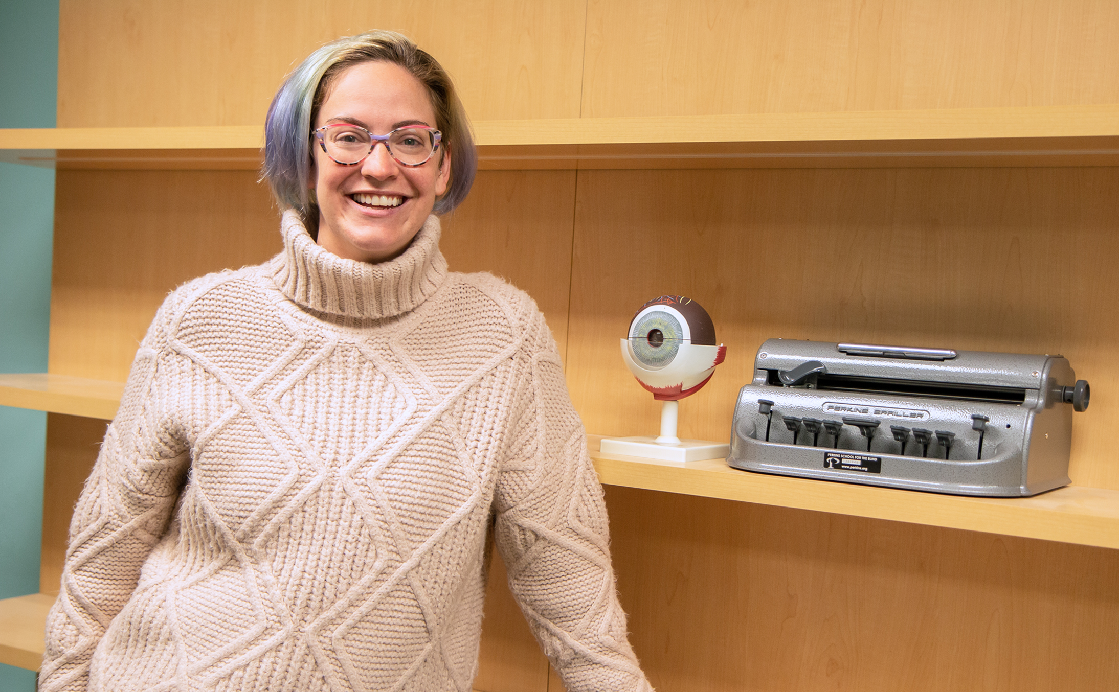 Researcher Mackenzie Savaiano stands in an office in front of visual impairment tools. 