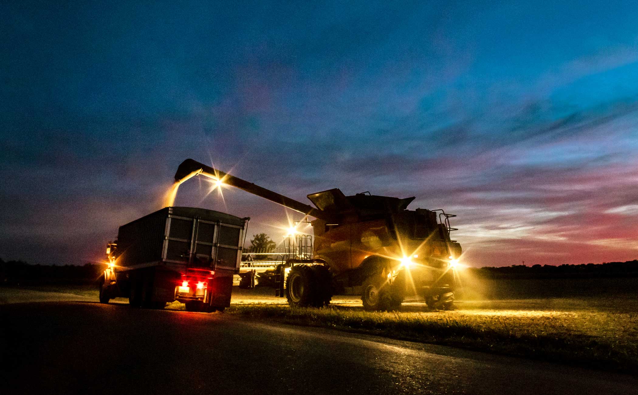 A combine dispenses grain into a feed truck during a nighttime harvest. 