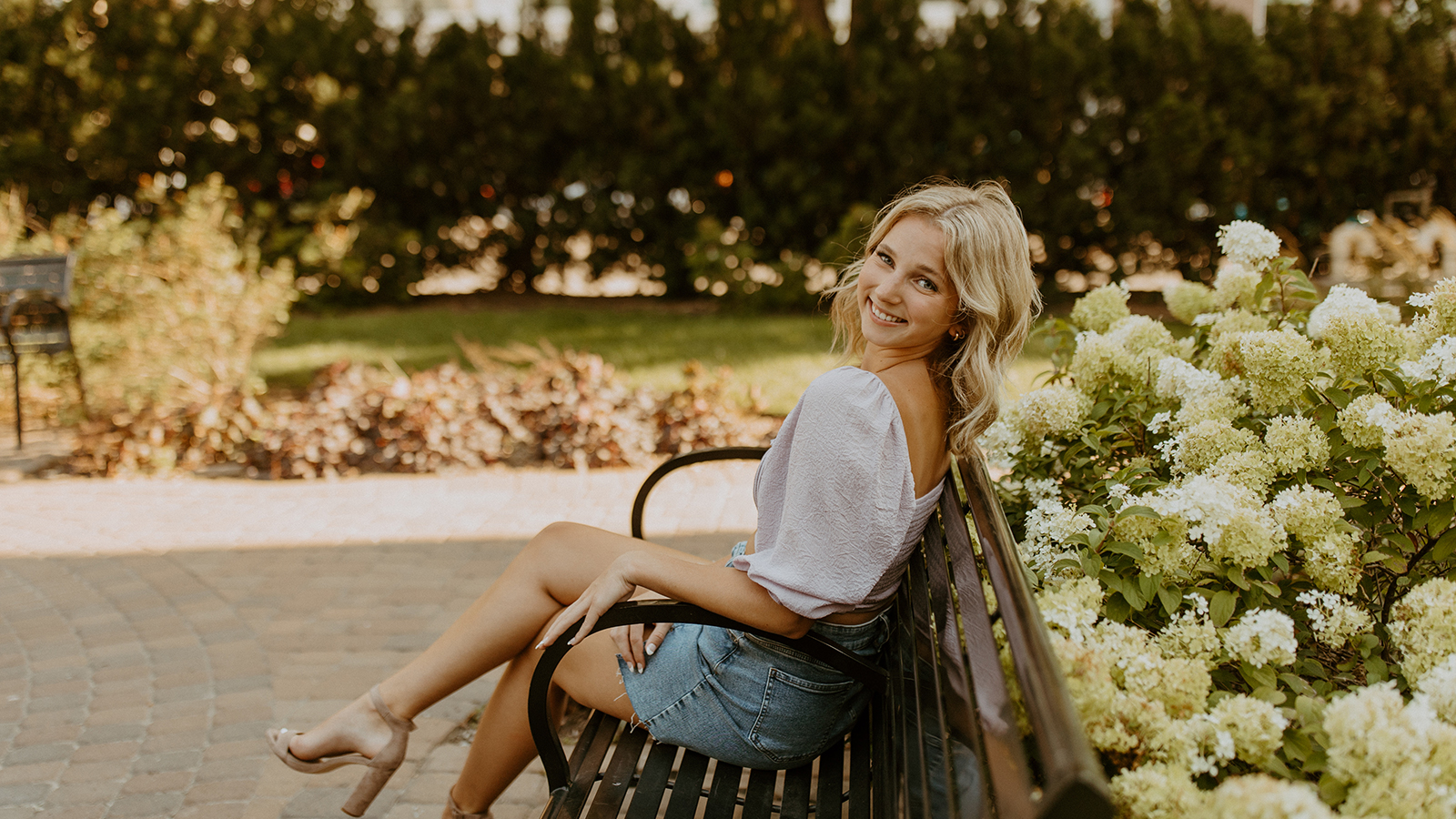 Hayley Corbridge sits on a bench with flowers blooming behind her