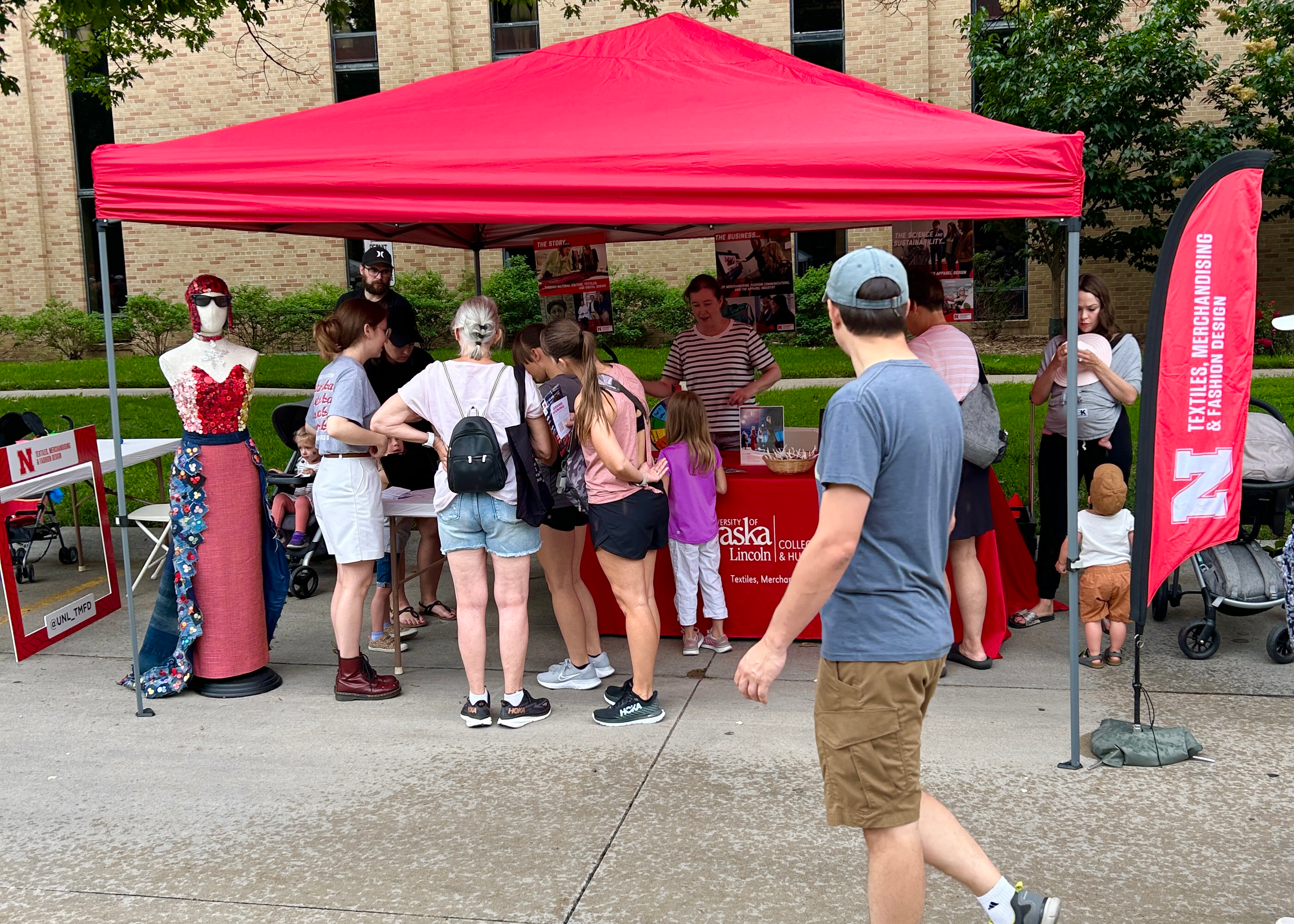 A large group gathers at the Textiles, Merchandising and Fashion Design red tent at East Campus Discovery Days. The display features the button dress community project. 