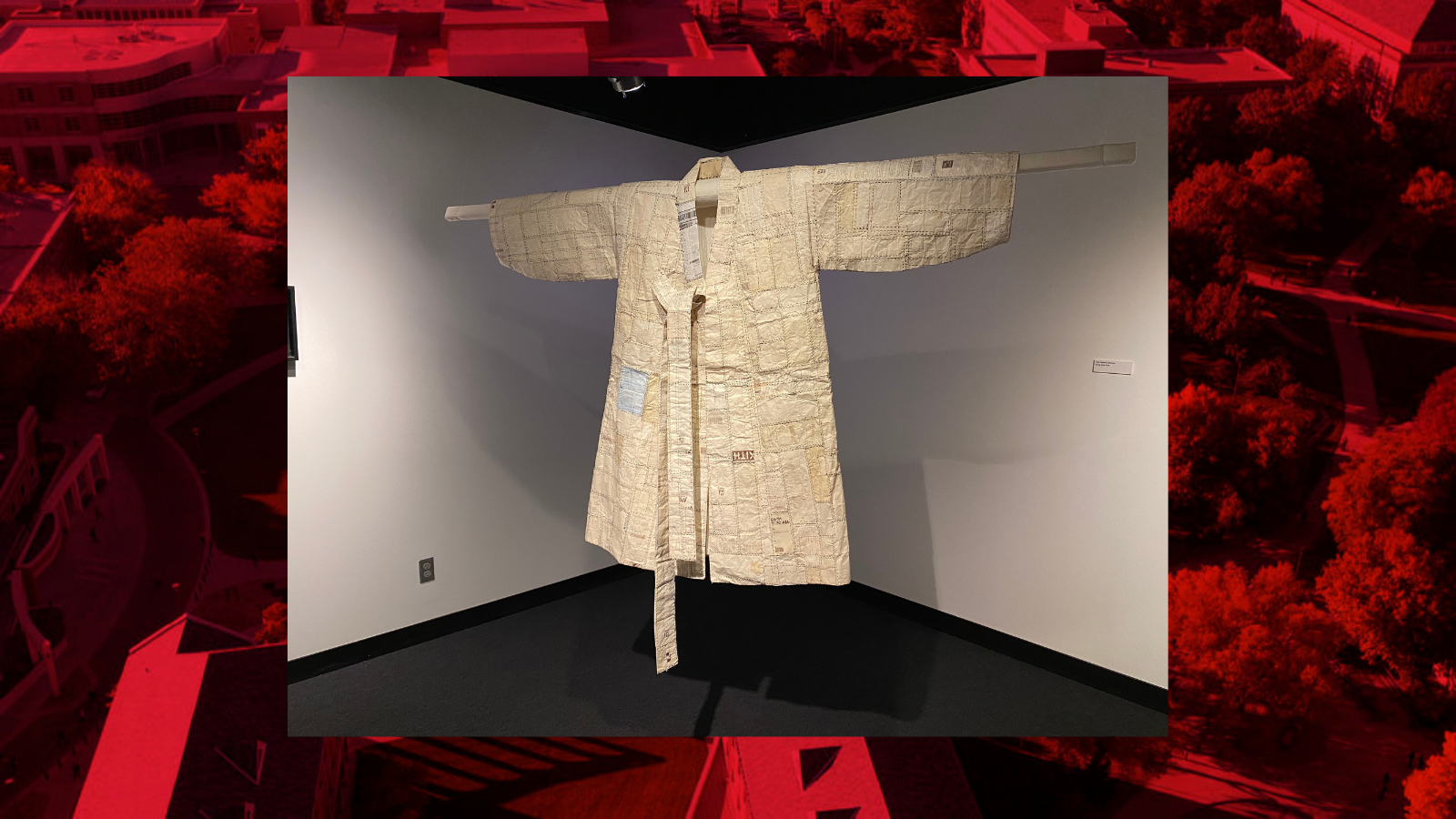 A robe constructed out of paper receipts hanging on display and lit in a studio space. 