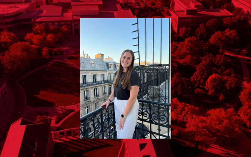 Lauren Mortenson stands on a balcony outdoors, with large ornate buildings behind her. That photo is placed on a red graphic. 
