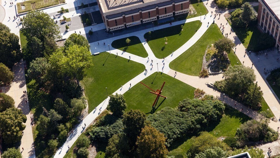 Overhead view of campus landscape. People walking on sidewalks that come together near the center of the photo. 
