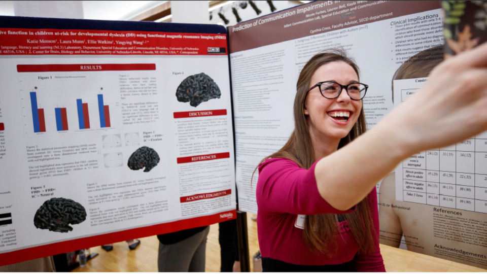 One person takes a selfie in front of a research poster. 
