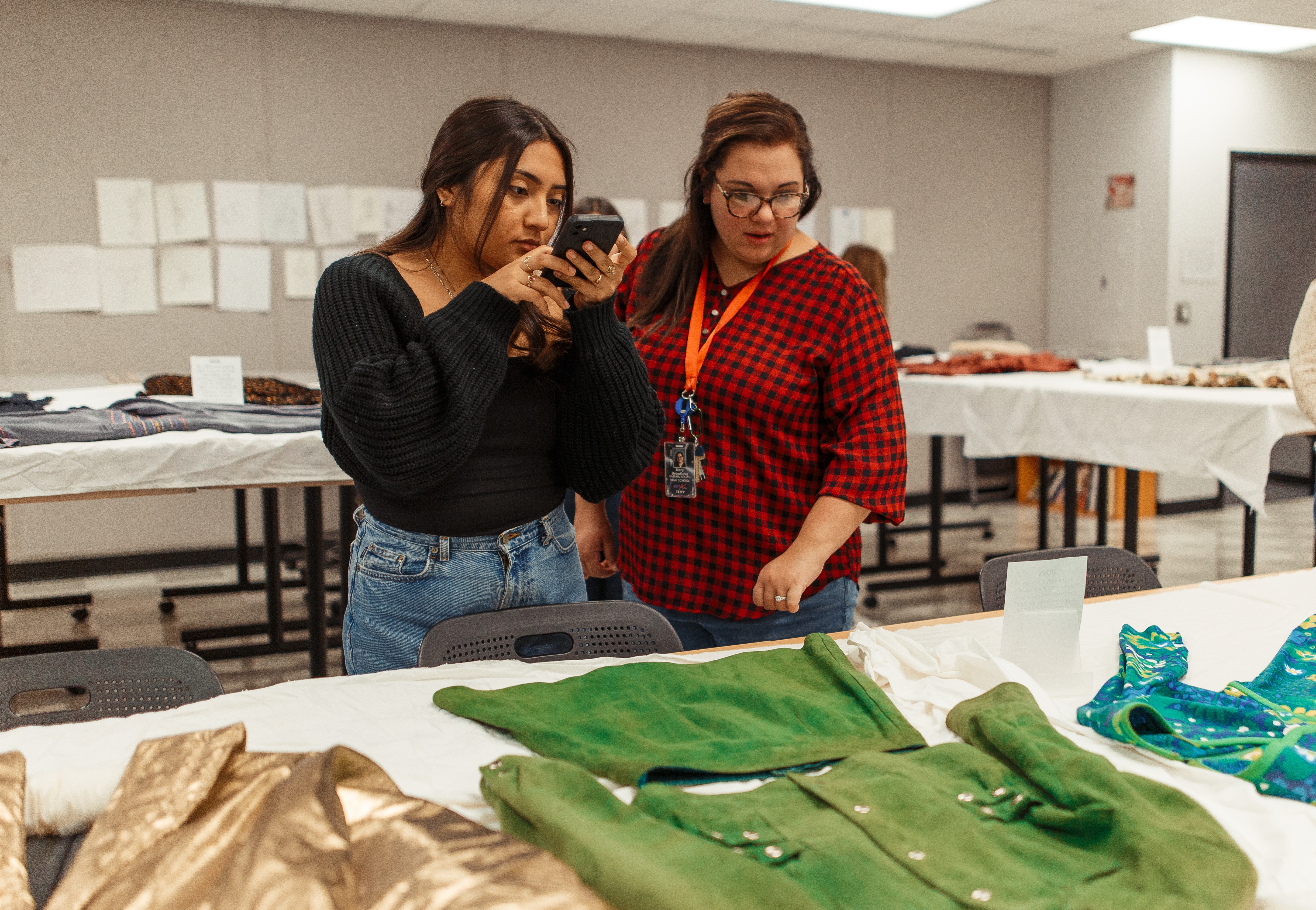 South High student takes a photo using her smartphone of a green garment from the Historical Textiles Collection housed in the department of Textiles, Merchandising & Fashion Design. 