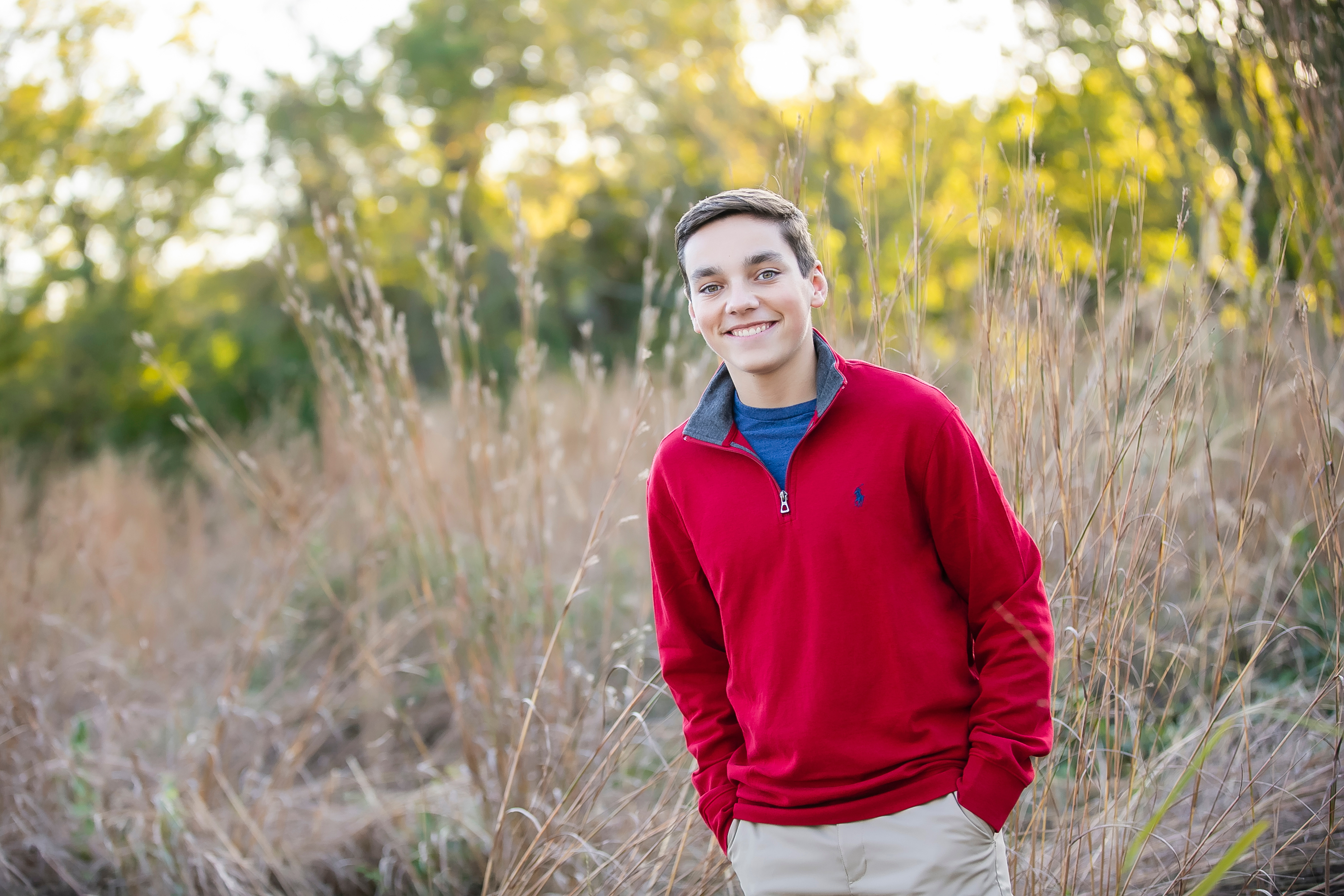 Grant Cline, wearing a red and blue sweatshirt, stands in a field of tall grass.