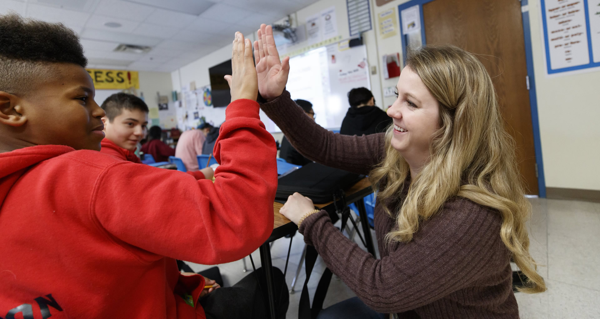 An adult and child smiling and high-fiving in a classroom setting. 