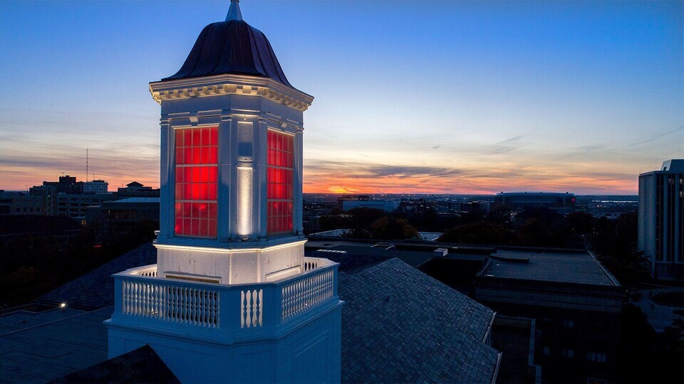 Overhead view of campus at sunset. The post of a white building is lit up and glowing red. 