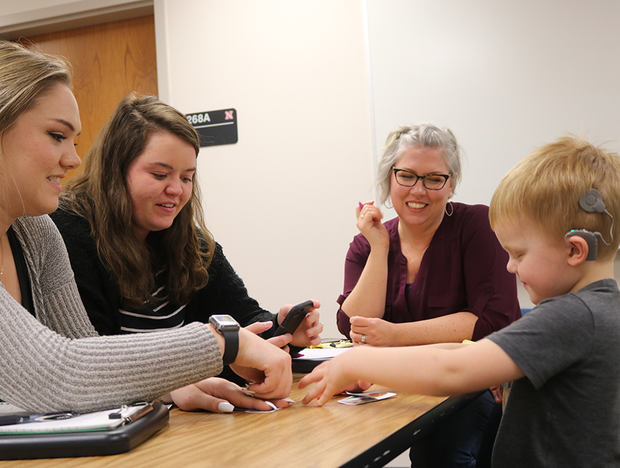 two graduate clinicians provide aural rehab to a young boy with a cochlear implant while a clinical supervisor observes