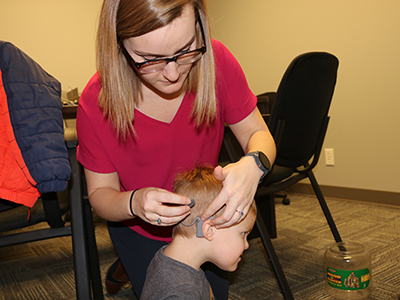 a Husker AuD student helps a young boy attach his cochlear implant
