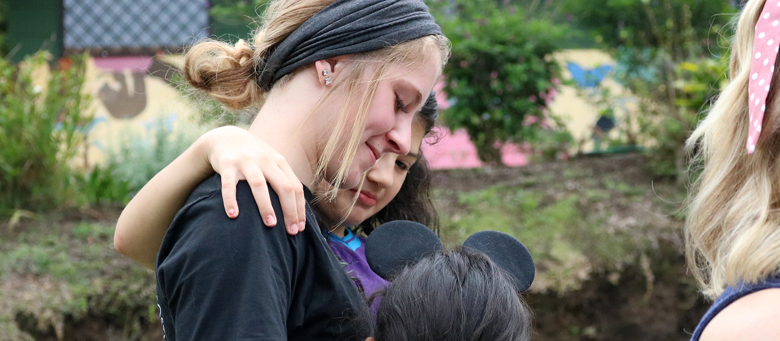 a Husker student hugs two elementary students at a school in Costa Rica