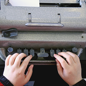 hands hover over a Braille typewriter