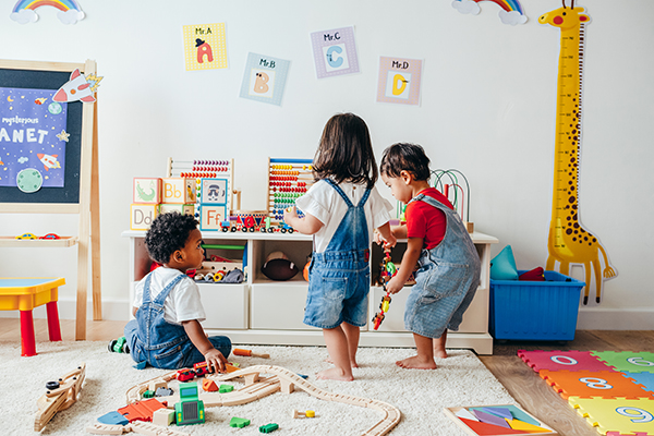 three children with their backs to the camera play in a room full of toys