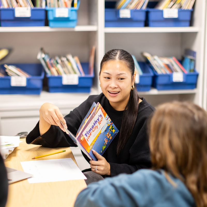 Teacher reading a children’s book to students at a table in a classroom.