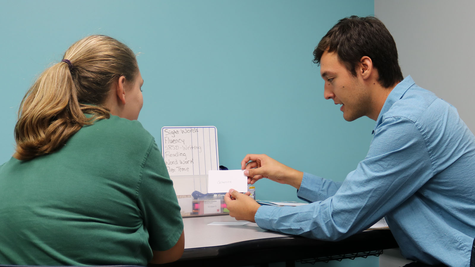 Two people seated across a table, engaging in a learning activity.