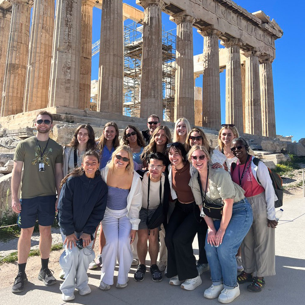 Group of people posing in front of the Parthenon on a sunny day.