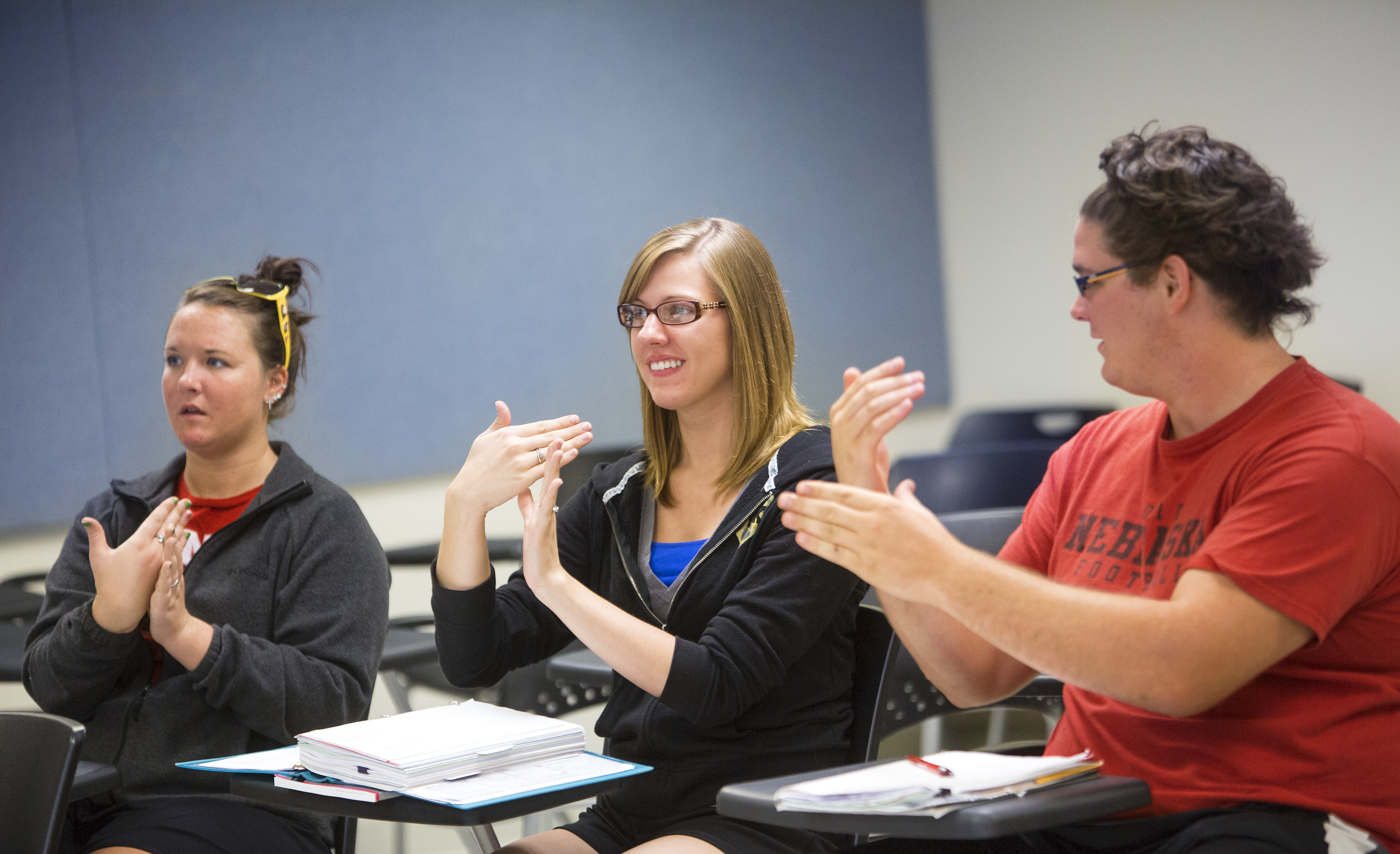 Students in a classroom engaged in sign language practice, seated with desks and notebooks.