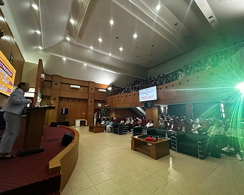 Theresa Catalano stands on stage giving a guest lecture to an auditorium full of students and faculty at Universitas Pendidikan Indonesia (UPI).