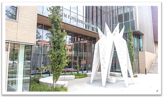 Modern building with tall glass windows, greenery, and a white geometric sculpture outdoors.