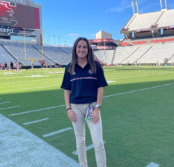 Woman standing on a football field under a clear blue sky.
