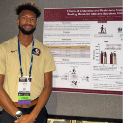 Man standing by a research poster about endurance and resistance training, wearing a lanyard and badge.