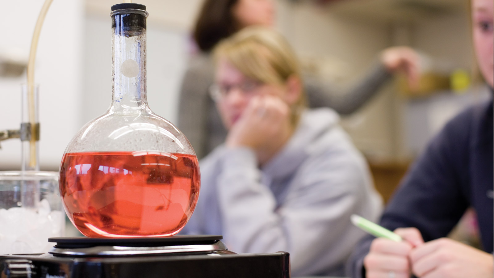 Beaker inside a lab with out of focus student in background.