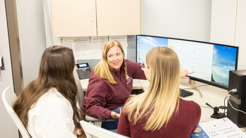 Group of three people around a computer.