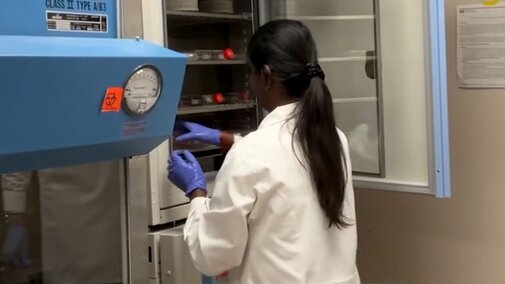 Scientist in a lab coat accessing lab equipment, wearing gloves, in a sterile environment.