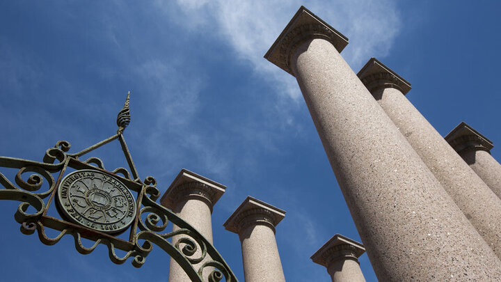 Large columns with an antique metal arch. Image looking up toward the blue sky.