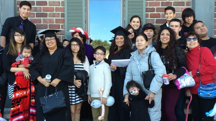 Two gradates in a cap and gown pose for a photograph with their families.