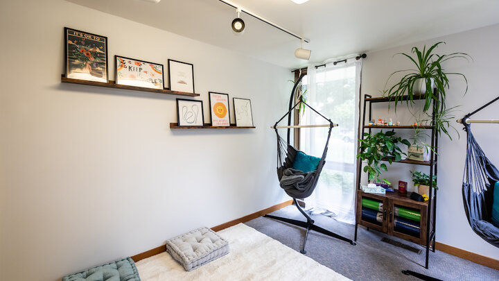 A well-lit room featuring pillows on the floor, cheerful artwork, and two hammock chairs. 