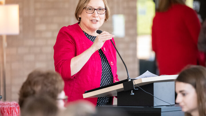 Mary Ann Johnson wearing a red jacket speaks at a podium. 