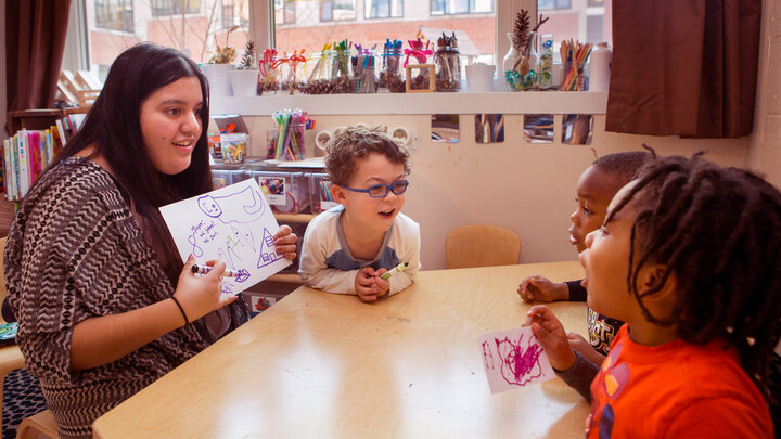 Teacher reading to students at a table in a school setting. 