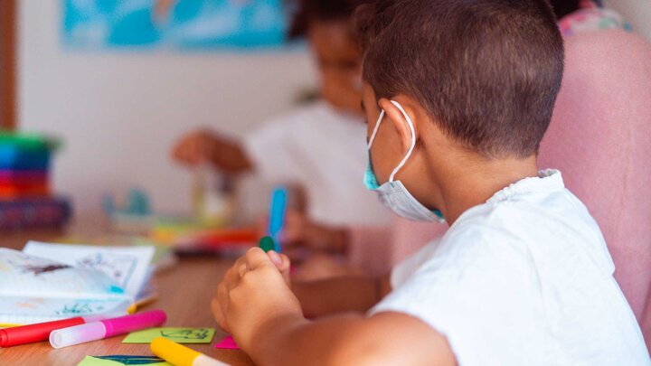 Young child sitting at a desk with colorful markers and papers. 