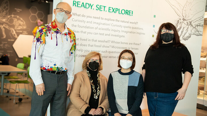 Four individuals posing for a photo. Two standing, two sitting in front of a display that reads 