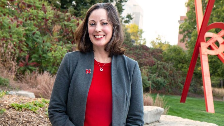 Individual standing outdoors in front of a red sculpture. Individual is wearing a red shirt and gray blazer. 