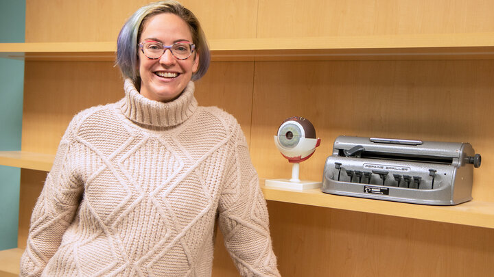 Researcher Mackenzie Savaiano stands in an office in front of visual impairment tools. 