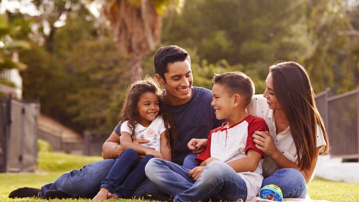 Two adults and two children sit in an outdoor setting and smile at each other. 