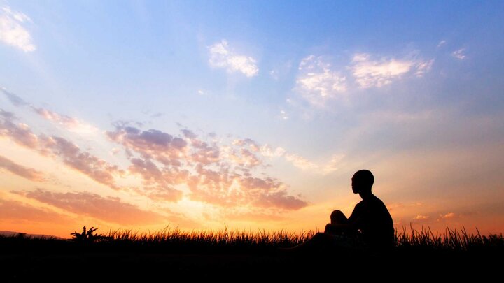 The silhouette of one individual sitting outdoors watching the sunset on top of a hill. 