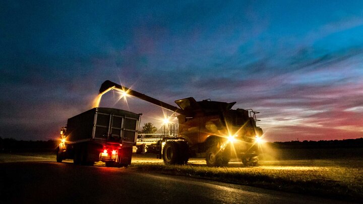 A combine dispenses grain into a feed truck during a nighttime harvest. 