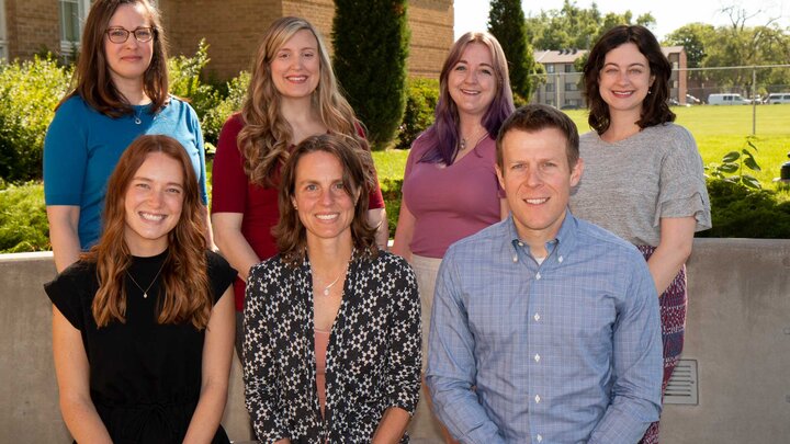 Two rows of adults outdoors posing for a photo. 