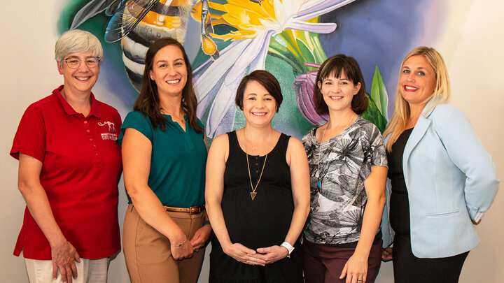 Five people dressed in business casual clothing stand in front of a colorful photo of an insect and a flower. 