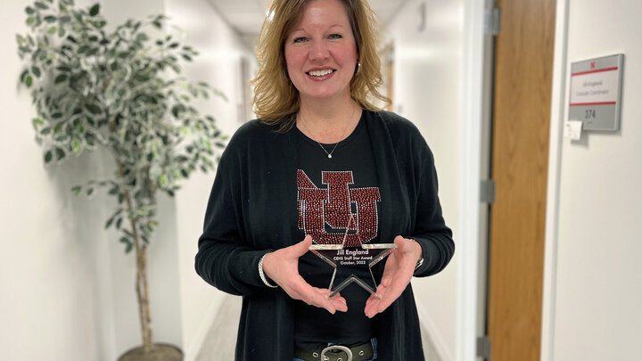 Jill England stands in a hallway holding her CEHS Staff Star Award. 